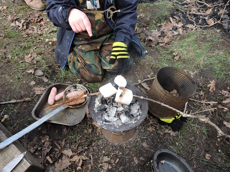 Close up of child cooking - Ladle & charcoal pot cooking sausages - Primary-School-Resources